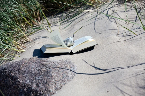 Читайте на пляже. Книга лежит открытой на песчаном пляже между дюнной травой — стоковое фото