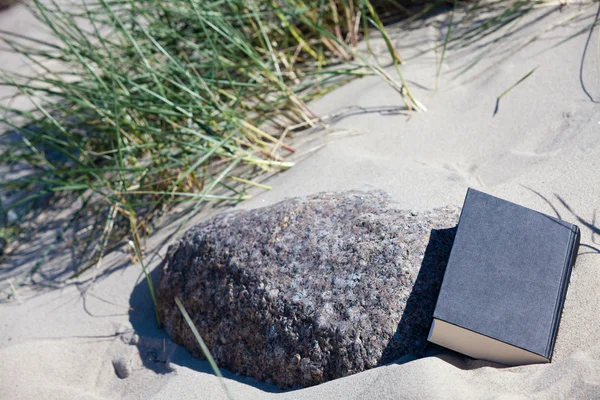 stock image A closed book lies in the sand at a stone