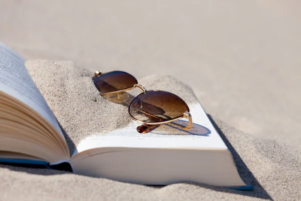 Vista de cerca de las gafas de sol se encuentra en un libro abierto en la playa —  Fotos de Stock