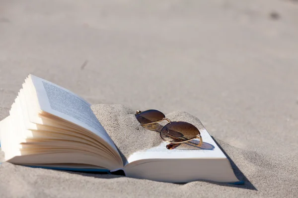 Sunglasses with brown tinted lenses lies on an opened book on the beach — Stock Photo, Image