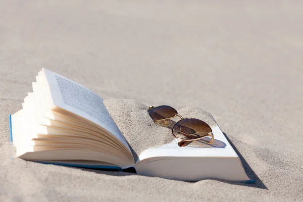 Sunglasses with brown tinted lenses lies on an opened book on the beach — Stock Photo, Image