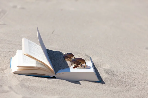 Óculos de sol com lentes de cor marrom jaz em um livro aberto na praia — Fotografia de Stock
