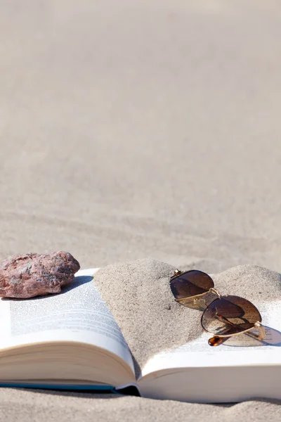 棕色茶色镜片的太阳镜躺在海滩上已打开的书 — 图库照片