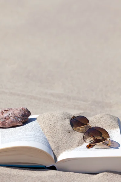 Napszemüveg, barna színezett lencsével fekszik egy nyitott könyv — Stock Fotó