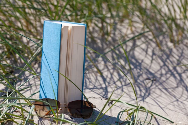 stock image A book with a sunglass lying in the sand in a dune