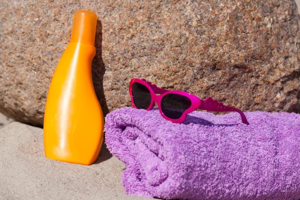 Asciugamano da bagno, crema solare e occhiali da sole sono su una roccia sulla spiaggia — Foto Stock