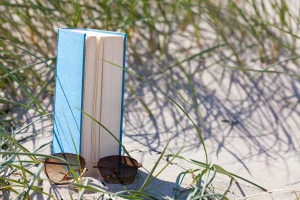 Bir kitap bir dune kum içinde yatan bir sunglass ile — Stok fotoğraf