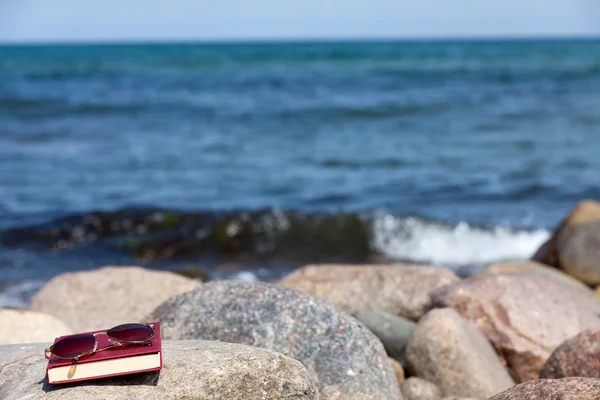 Sahilde bir kayada kapalı kitap koyu renkli Güneş gözlükleri ile yatıyor — Stok fotoğraf