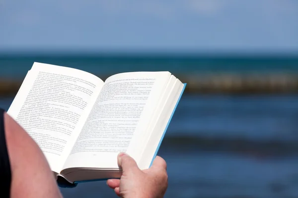 A person holds an open book in his hands and reads on the beach — Stock Photo, Image
