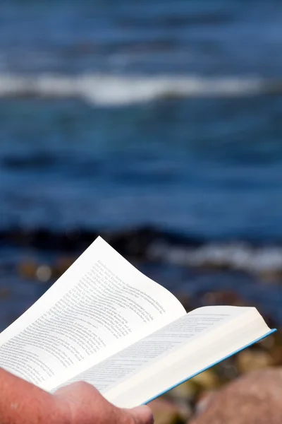 A person holds an open book in his hands and reads on the beach — Stock Photo, Image