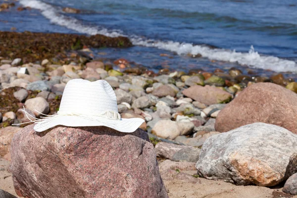 En vit stråhatt ligger på en klippa på stranden — Stockfoto