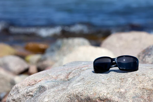 Солнечные очки в темных тонированных очках лежат на скале на побережье — стоковое фото