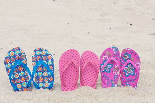 Three pairs bath slippers in a row stuck in the sand beach — Stock Photo, Image