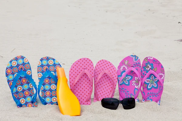 Três pares de chinelos de banho em uma fileira preso na praia de areia — Fotografia de Stock