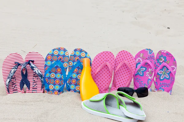 Four pairs bath slippers in a row stuck in the sand beach — Stock Photo, Image