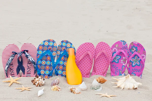 Quatro pares de chinelos de banho em uma fileira preso na praia de areia — Fotografia de Stock