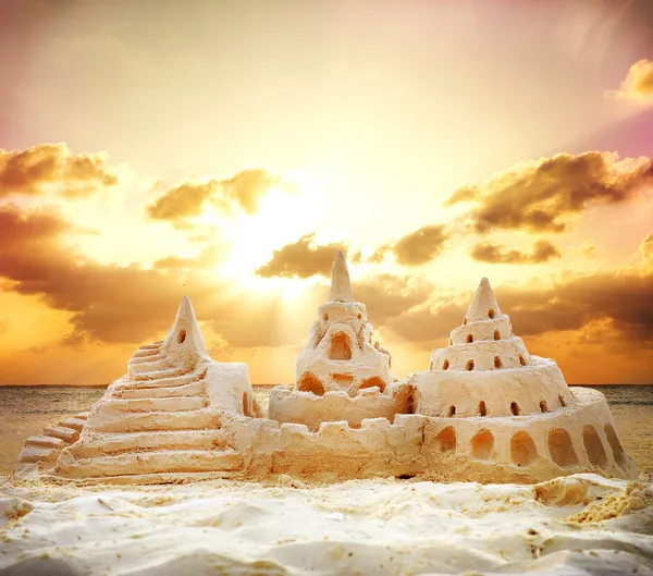 Castelo de areia sobre o pôr do sol na praia — Fotografia de Stock