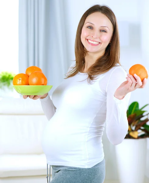 怀孕的年轻女子在家里吃水果 — 图库照片