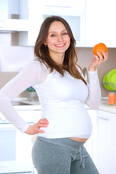 怀孕的年轻女子在家用厨房吃水果 — 图库照片