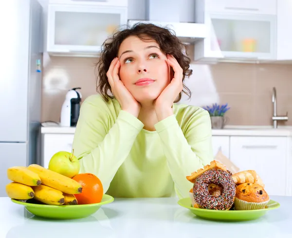 Beautiful Young Woman choosing between Fruits and Sweets Stock Image