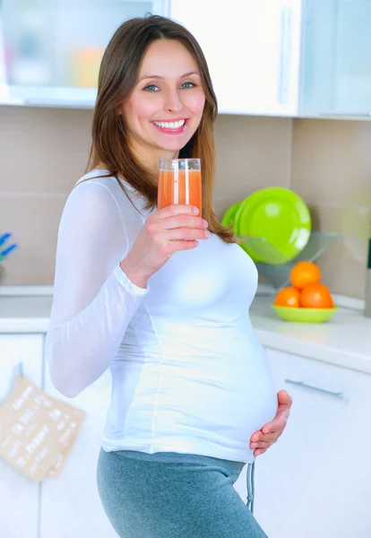 Giovane donna incinta che beve succo fresco a casa cucina Immagine Stock