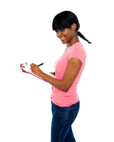 Smiling girl writing on clipboard — Stock Photo, Image