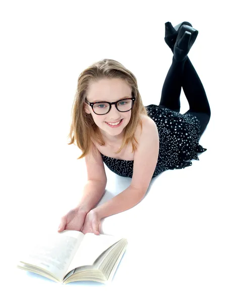 Улыбающаяся маленькая девочка лежит с открытой книгой — стоковое фото