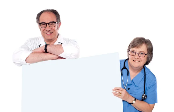 Two matured doctors holding white banner ad — Stock Photo, Image