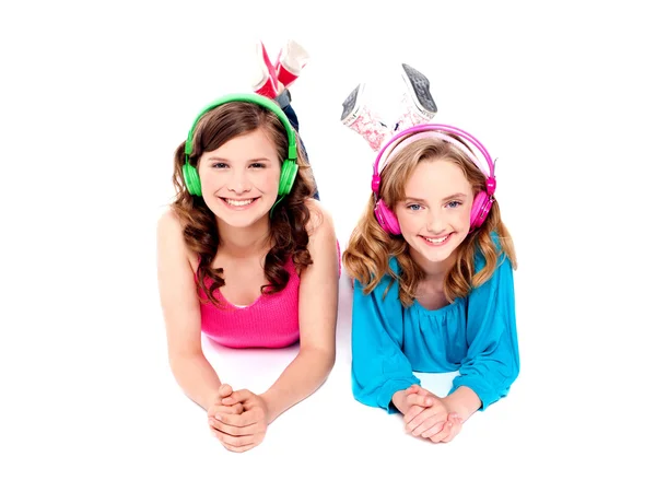 Zwei schöne Mädchen, die mit Kopfhörern auf dem Boden liegen — Stockfoto