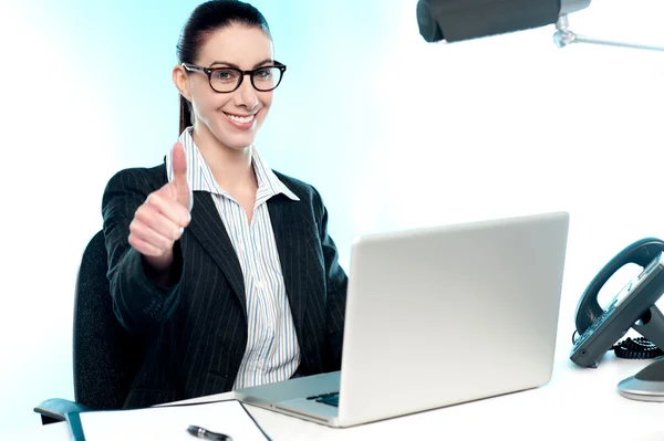 Young businesswoman sitting on desk gesturing thumbs up — Stock Photo, Image