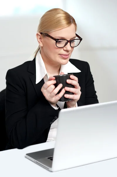 Executivo feminino olhando para laptop segurando caneca — Fotografia de Stock