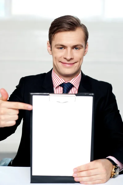 Smiling man pointing towards blank clipboard — Stock Photo, Image