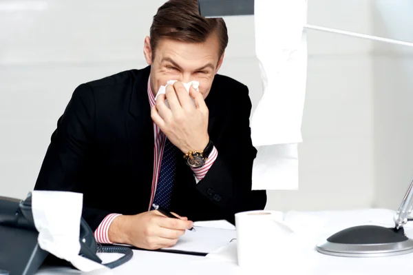 Profesional sentado en el escritorio estornudando en el tejido — Foto de Stock