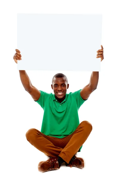 Siedzi młody człowiek posiadający biały pusty transparent — Zdjęcie stockowe