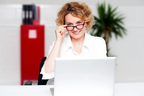 Mulher envelhecida segurando óculos trabalhando no laptop — Fotografia de Stock