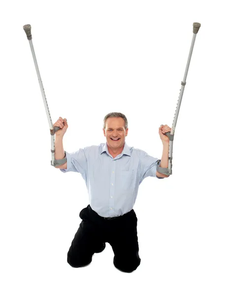 Stock image Cheerful senior man holding crutches upwards