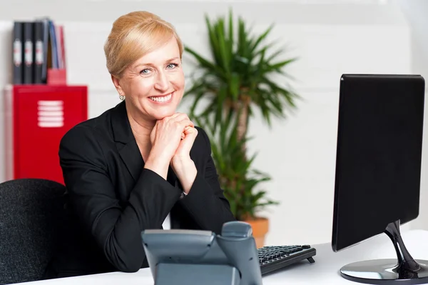 Aged businesswoman sitting with hands on chin — Stock Photo, Image