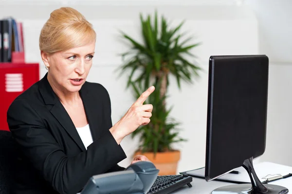 Angry woman indicating at computer led screen — Stock Photo, Image