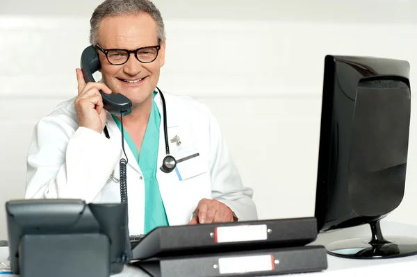 Médico idoso que atende chamada na frente da tela lcd — Fotografia de Stock