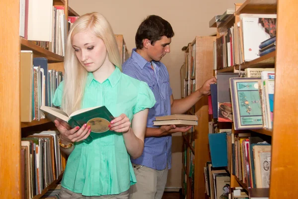 Νεαρή γυναίκα και άνδρα στη βιβλιοθήκη ψάχνει για ένα βιβλίο — Φωτογραφία Αρχείου