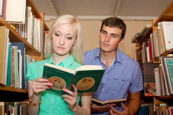 Молода жінка і чоловік в бібліотеці читають книгу — стокове фото