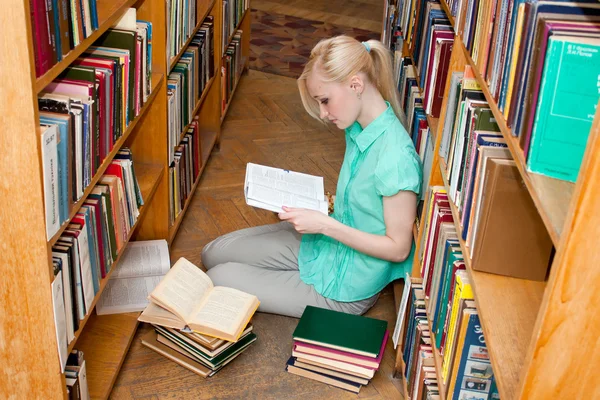 Estudante universitária lê um livro na biblioteca — Fotografia de Stock