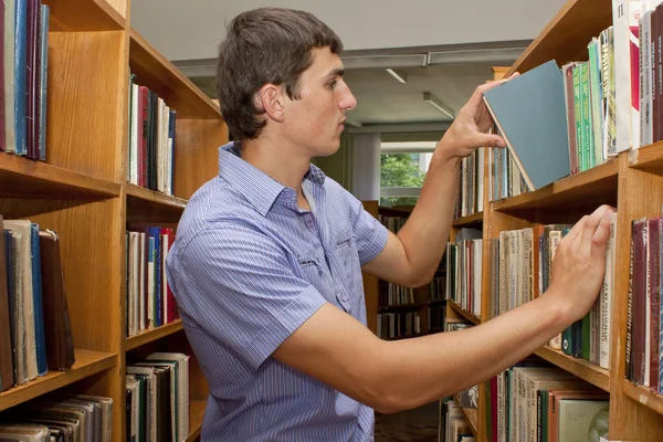 Молодий студент у бібліотеці шукає книгу — стокове фото