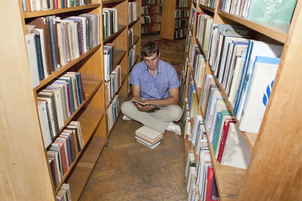 男子大学生は図書館で本を読み取ります — ストック写真