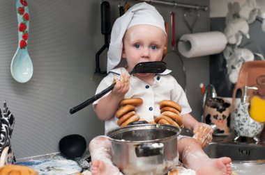 cook's şapkalı küçük çocuk bir tencereye bir masada oturuyor.