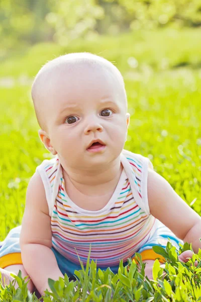 Little surprised baby sitting on the grass in park — Stock Photo, Image