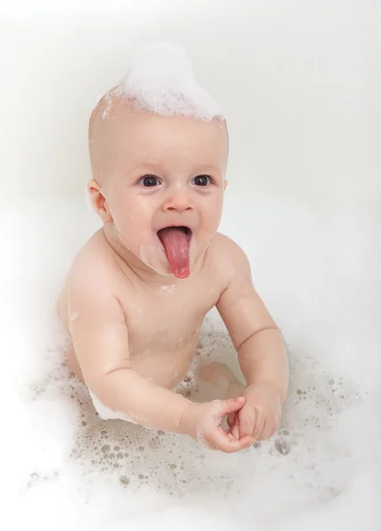 Pequeno bebê engraçado sentado na banheira em espuma branca — Fotografia de Stock