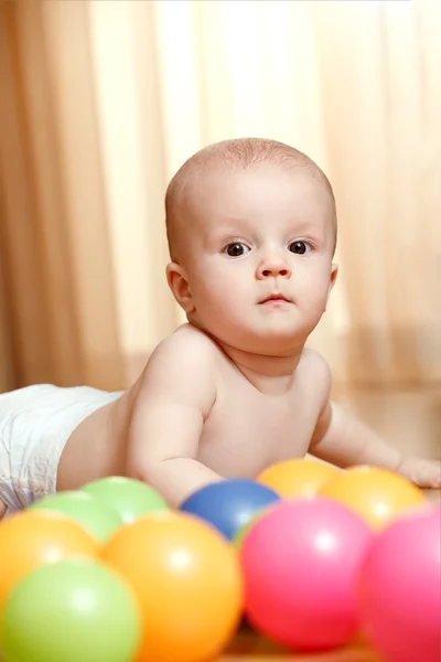 Pequeno bebê calmo deitado no chão com bolas coloridas — Fotografia de Stock