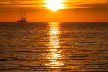Sail ship silhouette at sea and sun clipart
