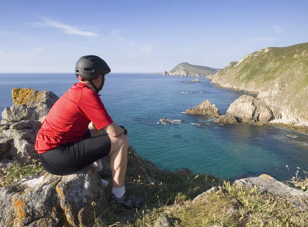 Ciclista sentado, olhando para uma paisagem costeira — Fotografia de Stock